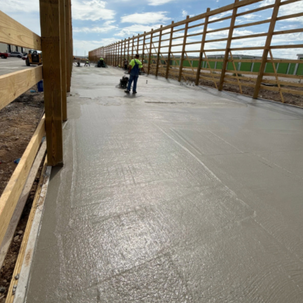 Worker finishing a freshly poured concrete floor at a commercial construction site.
