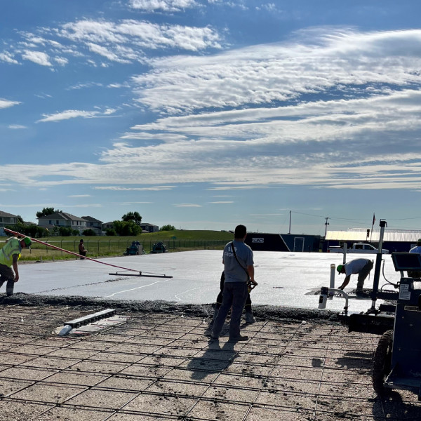 Workers pouring and leveling a concrete slab at a commercial construction site.