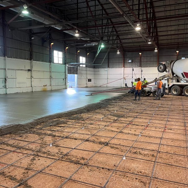 Workers pouring and finishing a concrete floor inside an industrial warehouse.