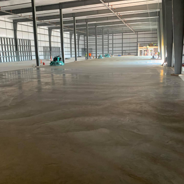 Smooth concrete floor finished inside a large industrial warehouse with steel structural columns.