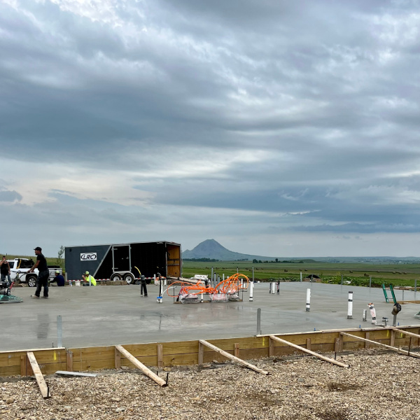 Concrete foundation slab at a commercial construction site with wooden formwork and plumbing installations.