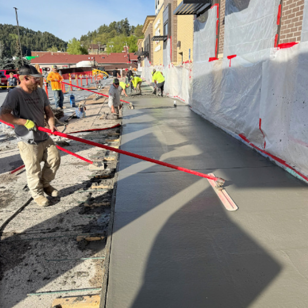 Workers pouring and leveling fresh concrete for a commercial sidewalk alongside a building.