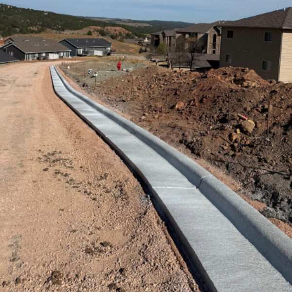 Newly installed concrete curb and gutter along a residential neighborhood road under construction.