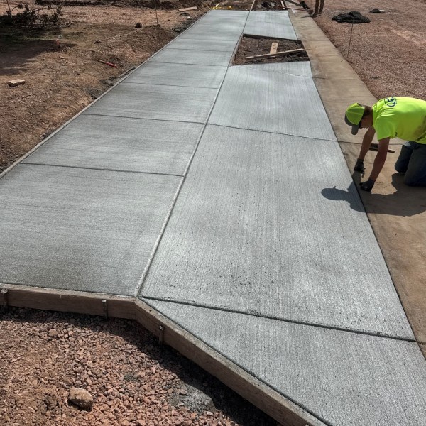 Worker finishing a newly installed concrete sidewalk with a smooth, textured surface at a residential construction site.