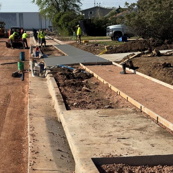 Workers installing a concrete sidewalk alongside a curb at a commercial construction site.