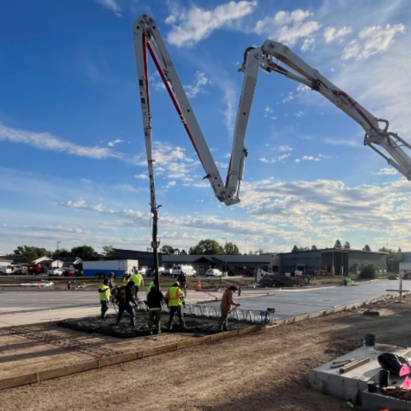 Workers pouring concrete using a boom pump truck at a commercial construction site.
