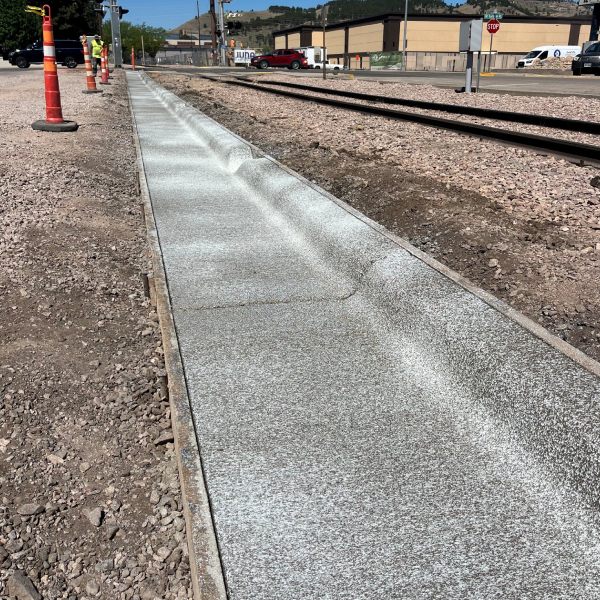 Newly finished concrete sidewalk with a textured surface along a commercial roadside.