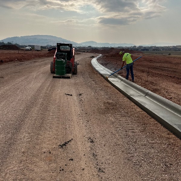 Worker finishing a newly poured concrete curb along a roadway at a commercial construction site.