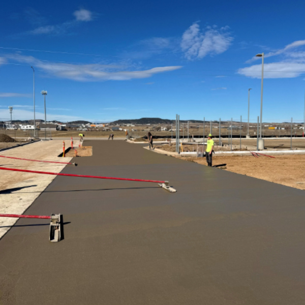 Workers leveling freshly poured concrete pavement at a commercial construction site.