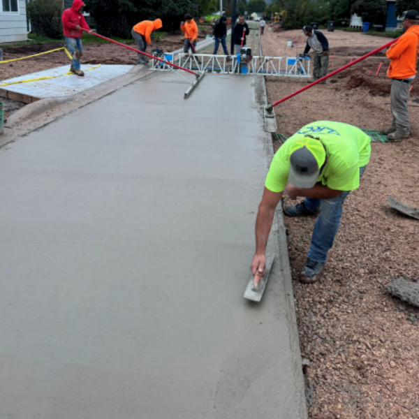 Workers leveling and smoothing freshly poured concrete for a driveway at a residential construction site.