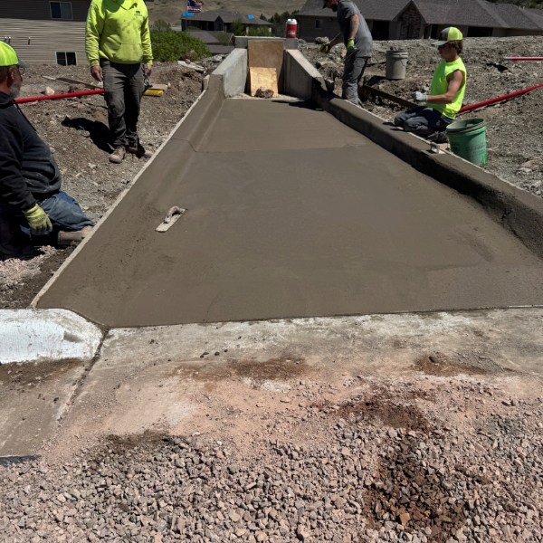 Workers finishing a freshly poured concrete driveway with wooden formwork at a residential construction site.